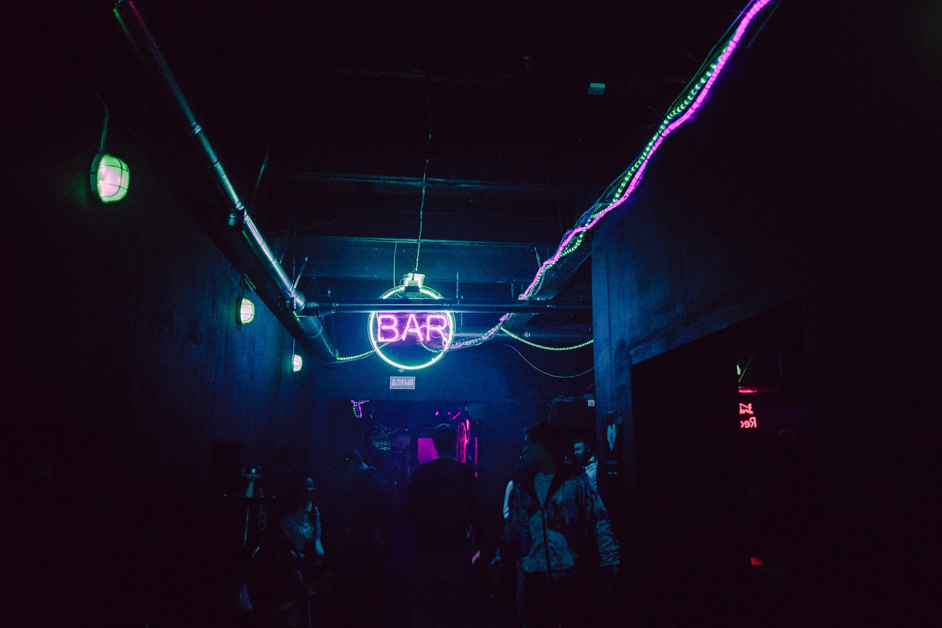 Imagen de un club a oscuras con luces de color neón rosa y amarillo y un letrero en el centro que dice "Bar"