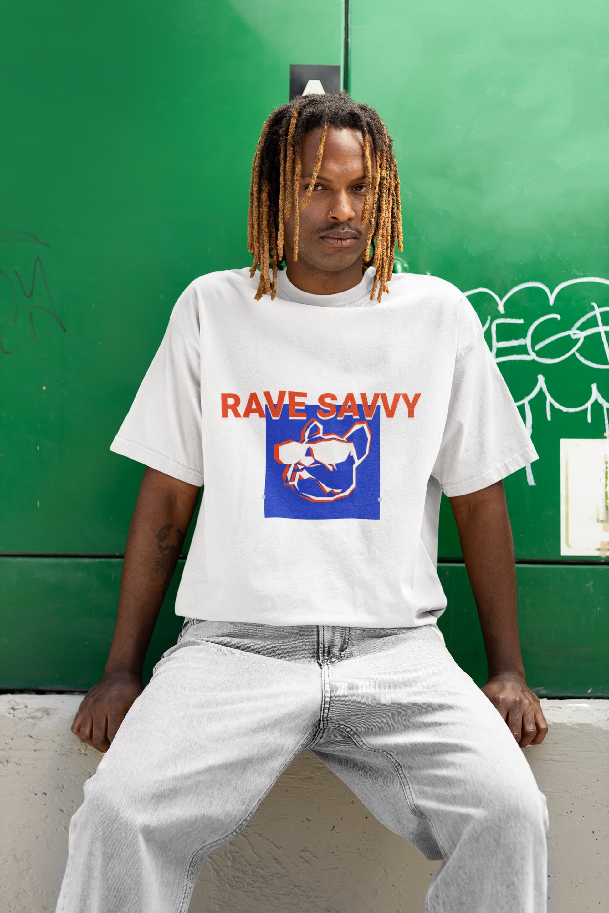 Picture of black man sitting with a green background wearing the white oversize "Bulldog" T shirt depicting the logo and the words "rave savvy"