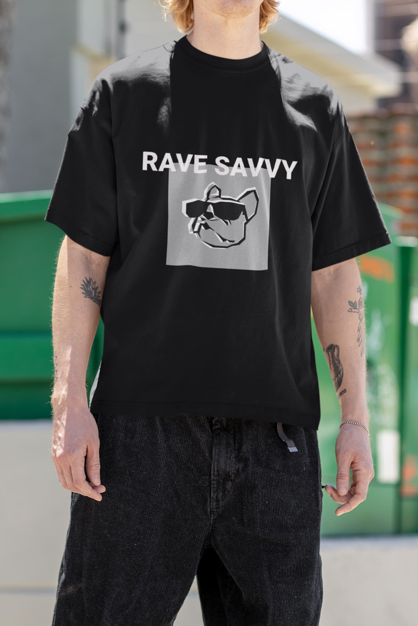 Chest picture of a white model with arm tattoos wearing the black oversize "Bulldog" T shirt depicting the logo and the words "rave savvy"