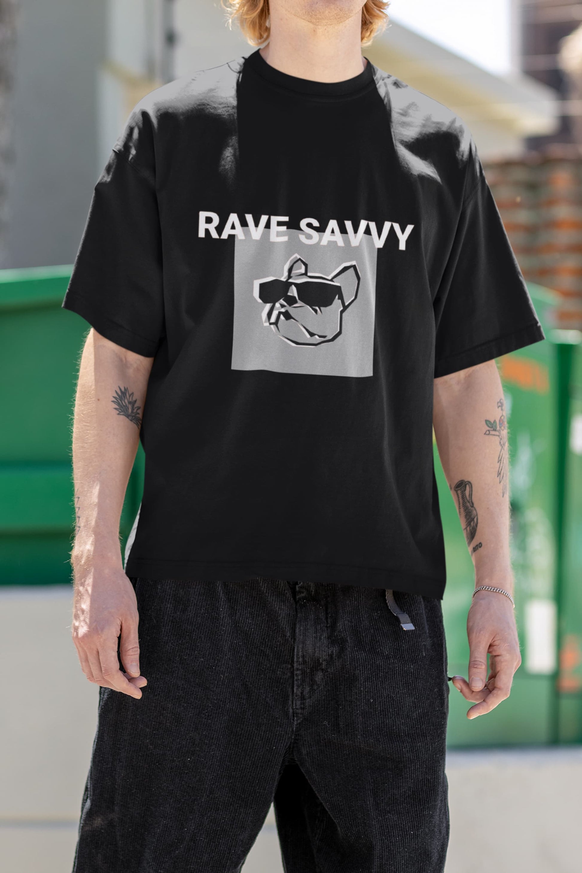 Chest picture of a white model with arm tattoos wearing the black oversize "Bulldog" T shirt depicting the logo and the words "rave savvy"